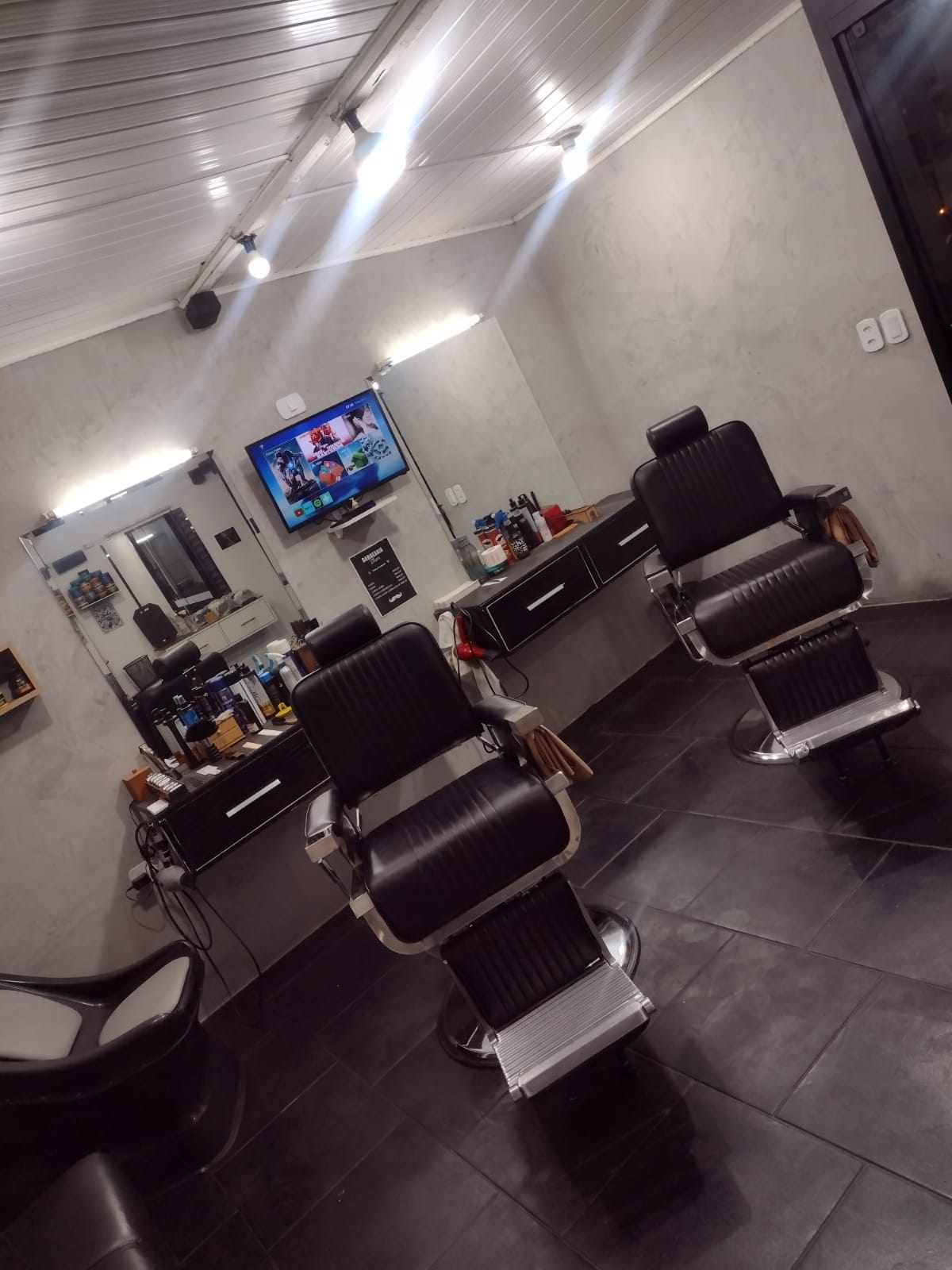 Ambiente interno da Barbearia Thom, com cadeiras de atendimento e TV na parede